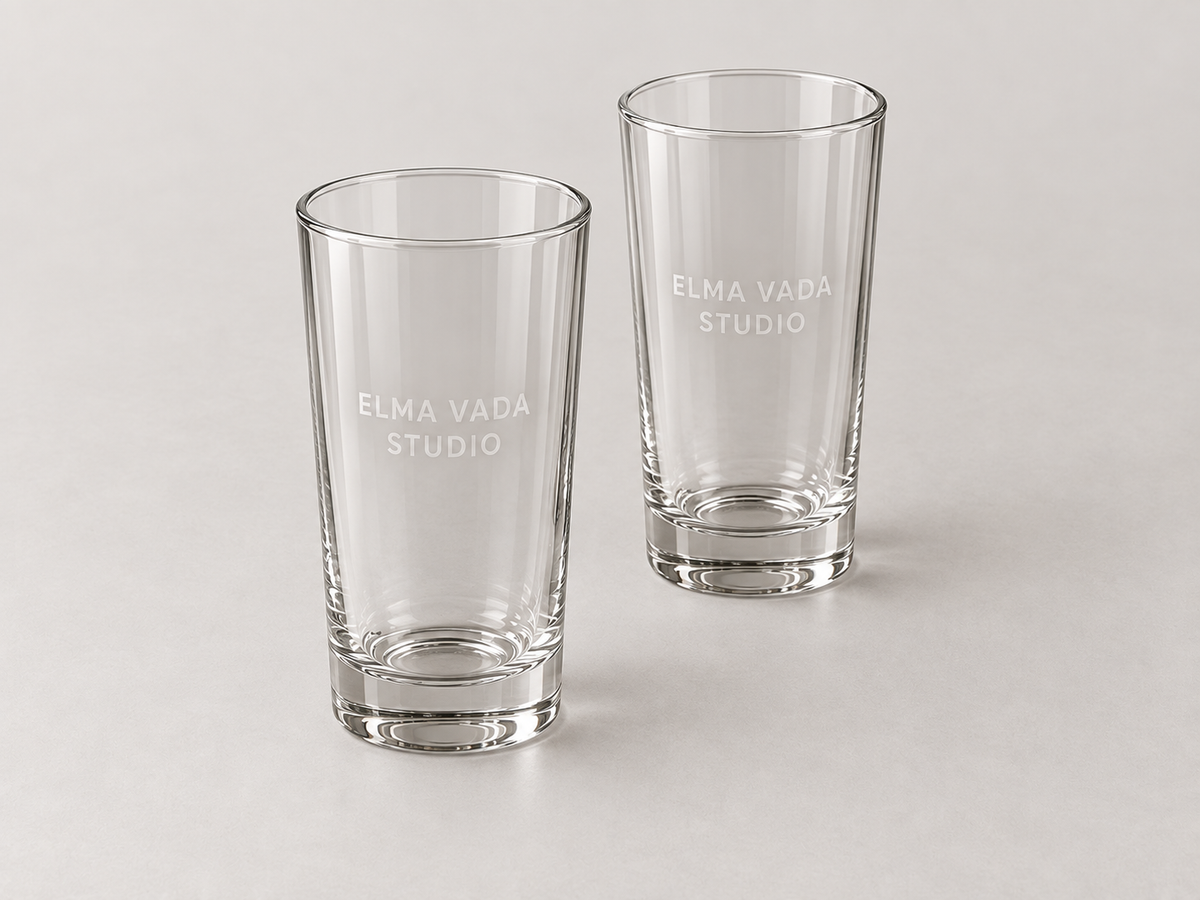 Two tall clear glasses with heavy bases and frosted Elma Vada Studio lettering.