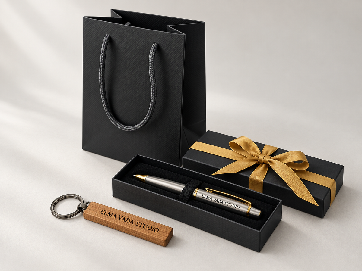 Engraved pen in a black gift box beside a wooden keychain, gold ribbon and black gift bag.