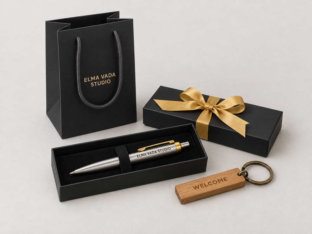 Engraved silver pen in a black box with gold ribbon, a gift bag and a wooden Welcome keychain.
