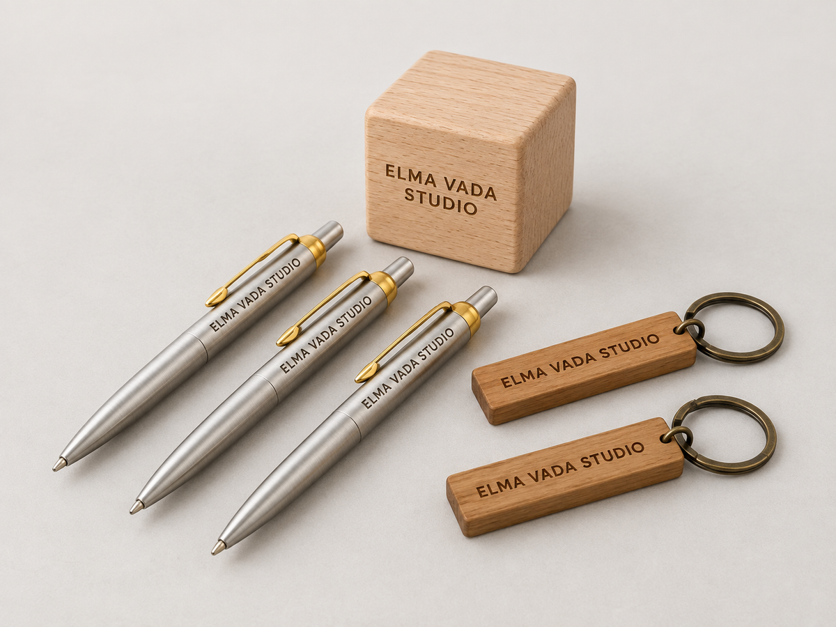 Silver metal pens, wooden keychains and a wooden desk cube engraved with Elma Vada Studio.