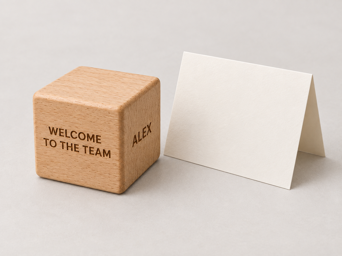Light wooden cube engraved Welcome to the Team and Alex beside a blank folded card.