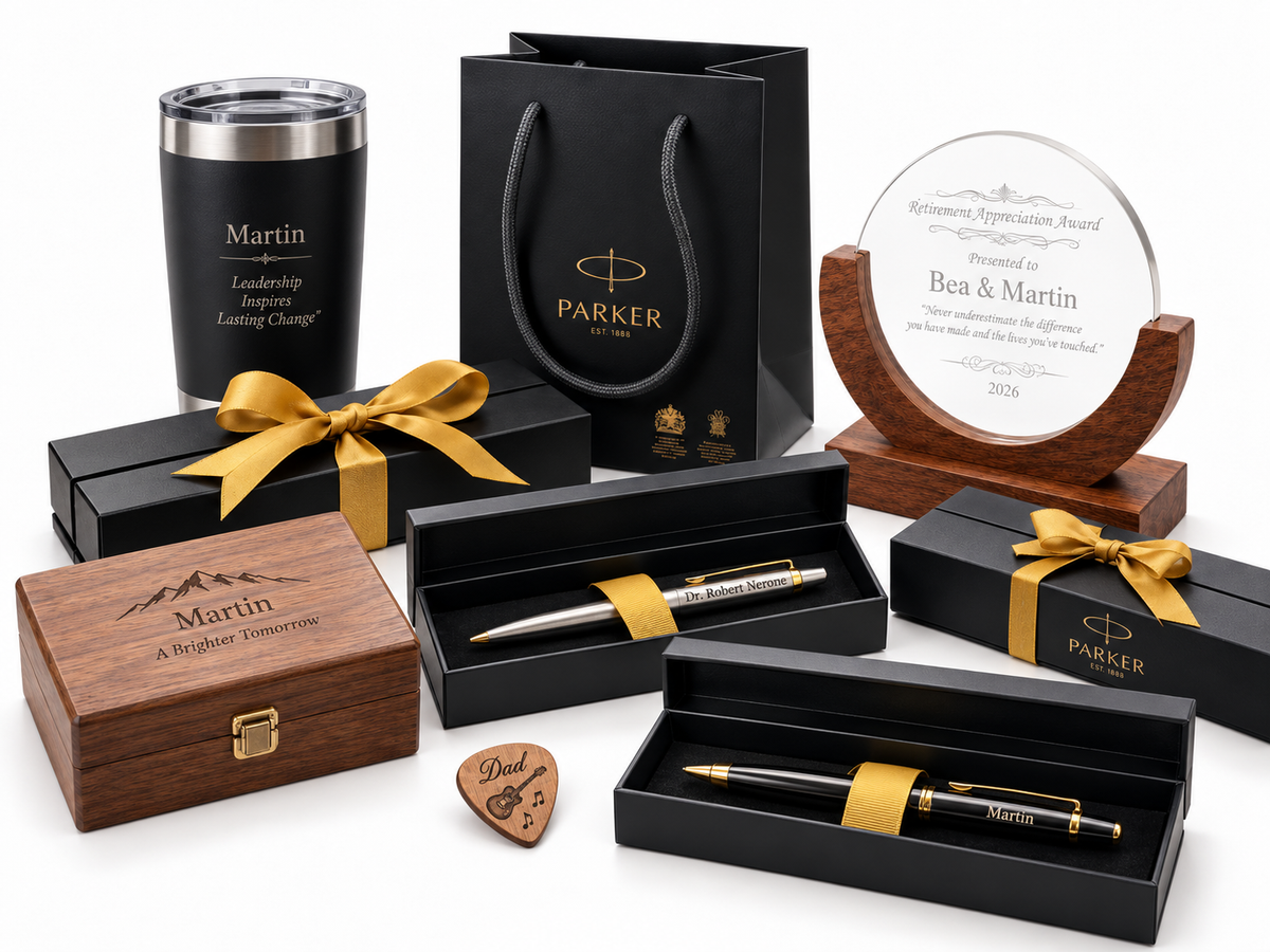 Personalized client gift set with engraved pens in presentation boxes, a custom tumbler, a wooden keepsake box, an engraved guitar pick and a clear recognition award arranged together for executive and corporate gifting.