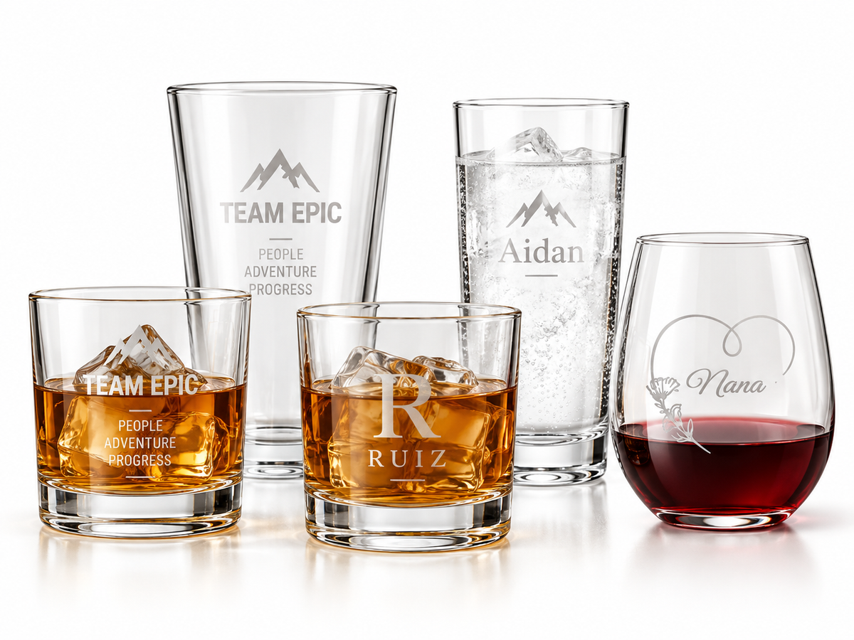 Assorted engraved glass gifts including personalized tumblers, a tall glass and a stemless glass with custom names and Team Epic branding on a white background.