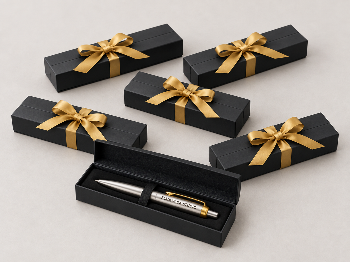 Five black boxes with gold bows behind an open box holding an engraved silver pen.